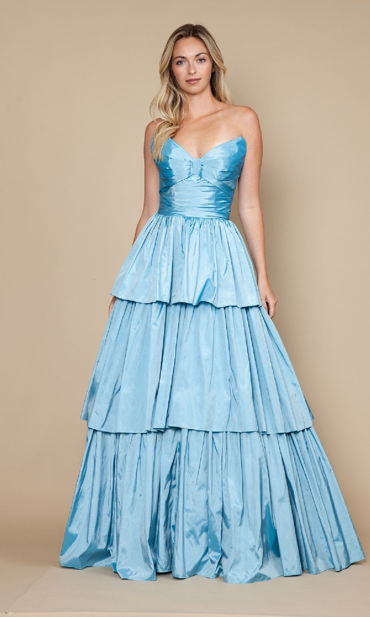 A woman poses against a tan background in the Long Prom Dress: Poly USA 9694, a light blue strapless, tiered A-line dress with a fitted bodice and full skirt.